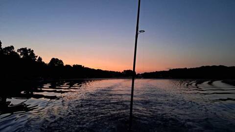 Sonnenuntergang über dem See, Blick vom Boot mit Angelrute