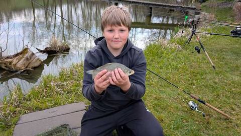 Junge zeigt einen Fisch am Ufer des Furthweihers