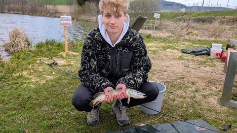 Jugendlicher hockt mit einem Fisch im Gras
