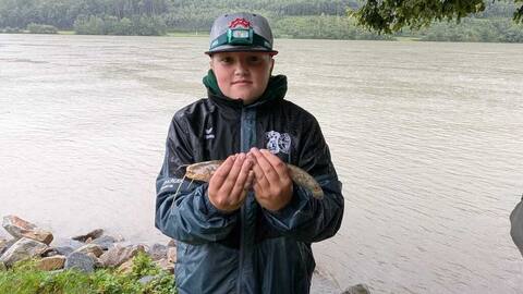 Jungangler zeigt einen gefangenen Fisch am Donauufer