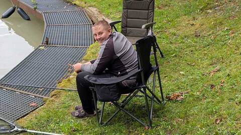 Jugendlicher sitzt im Campingstuhl am Steg und angelt